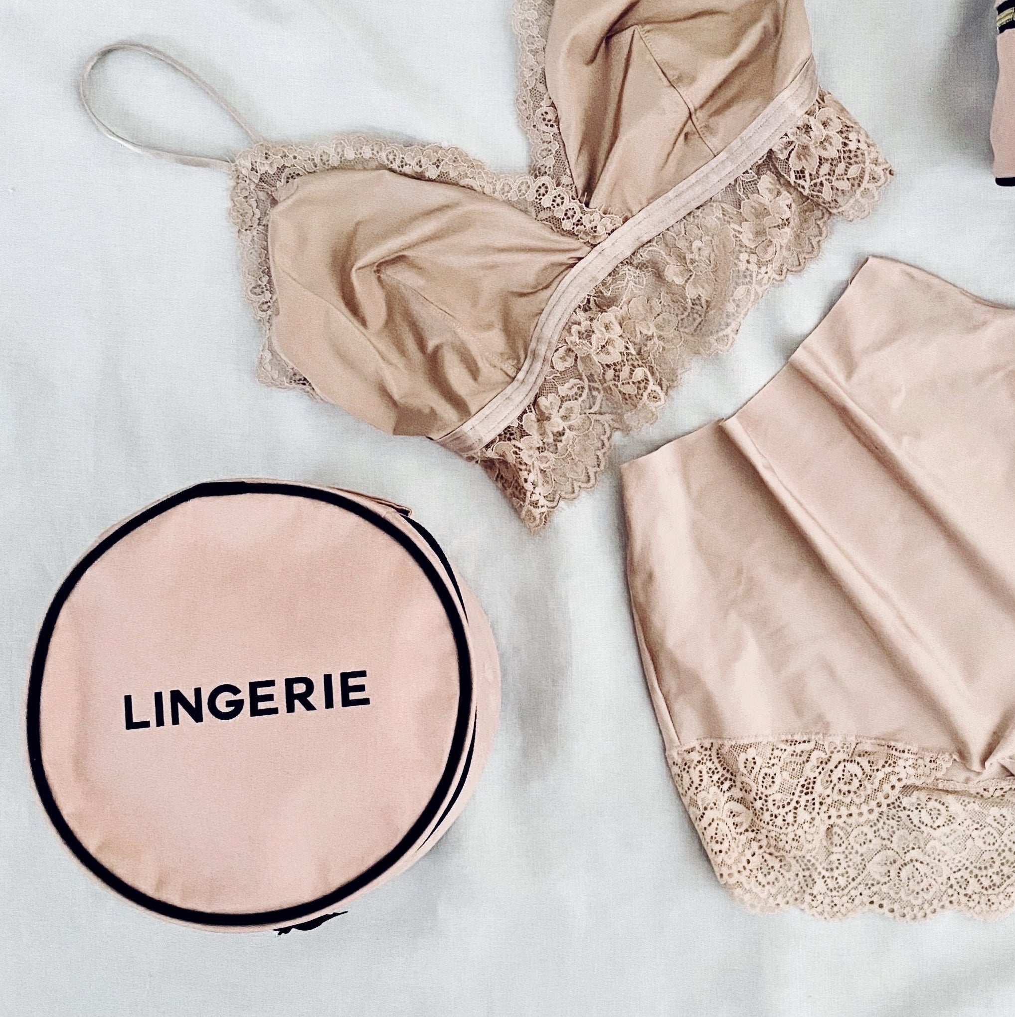 Bag-all Round Lingerie Case in blush pink shown with matching lace lingerie set, showcasing its perfect size and elegant design for organizing delicate undergarments while traveling