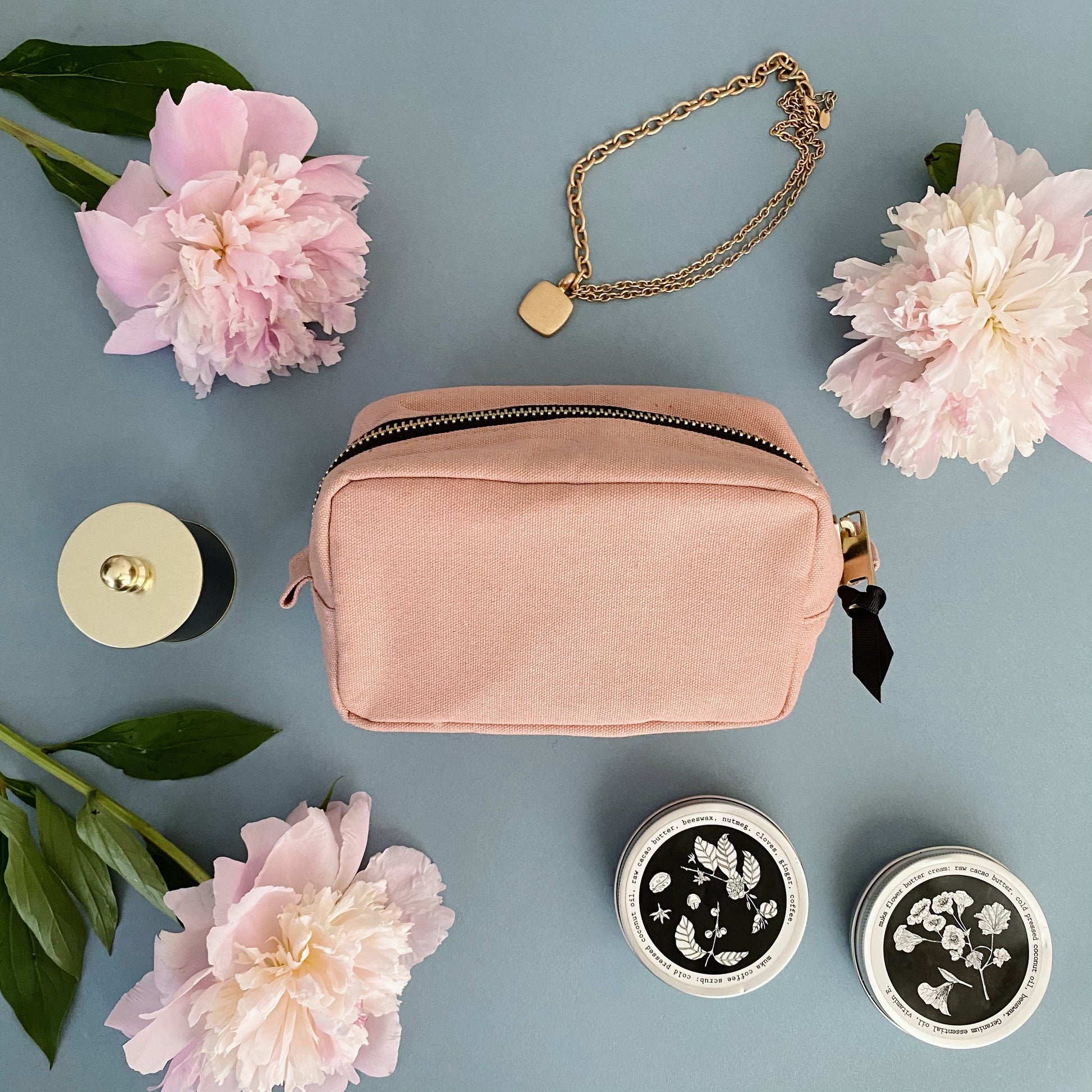 Bag-all Small Toiletry Pouch in pink blush canvas, styled with pink peonies and gold accessories. Compact travel-friendly design with zipper closure and wipeable interior for organizing essentials.