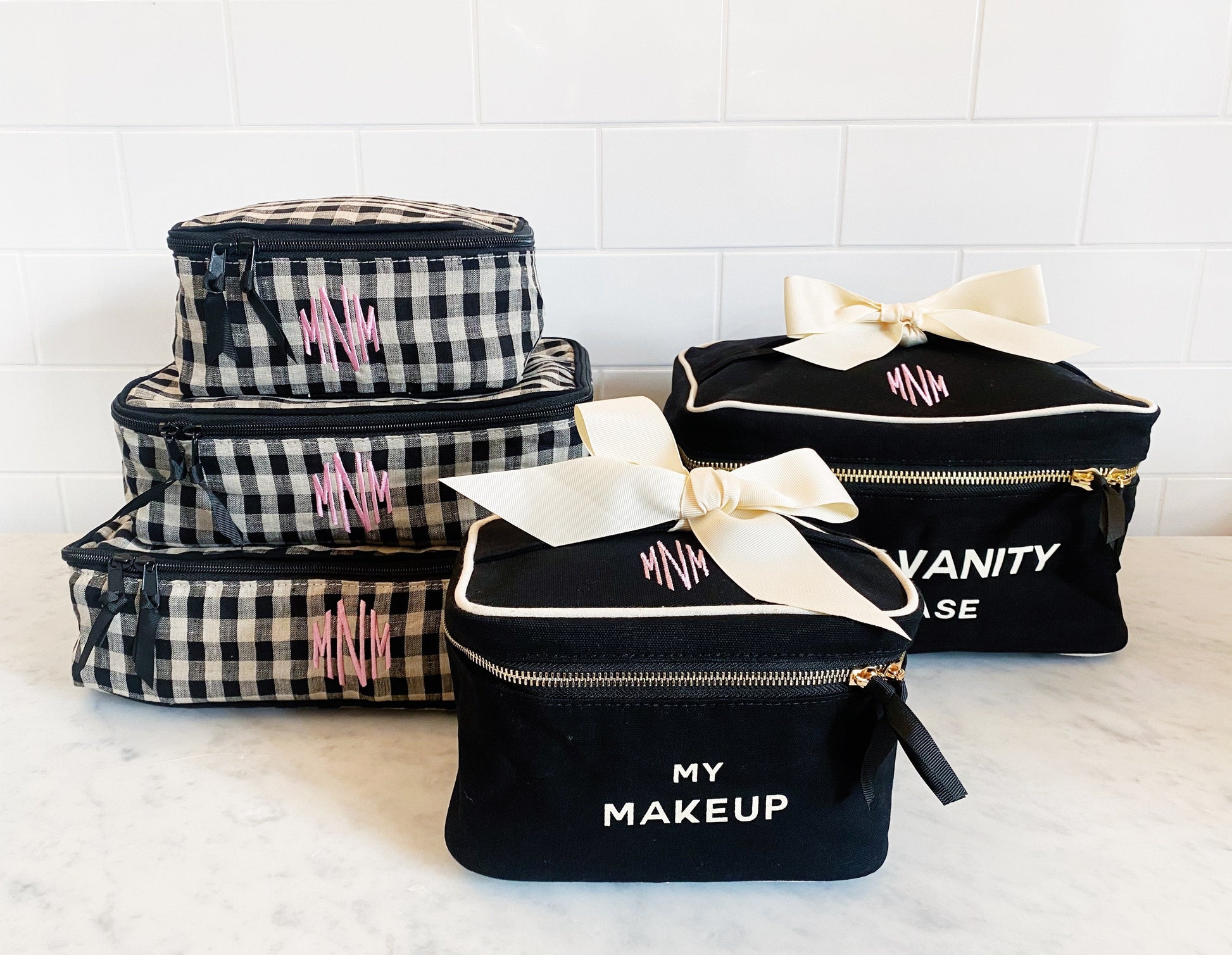 Bag-all personalized monogram makeup and vanity cases in black and gingham patterns with pink initials and cream bows, perfect for organizing cosmetics and travel essentials