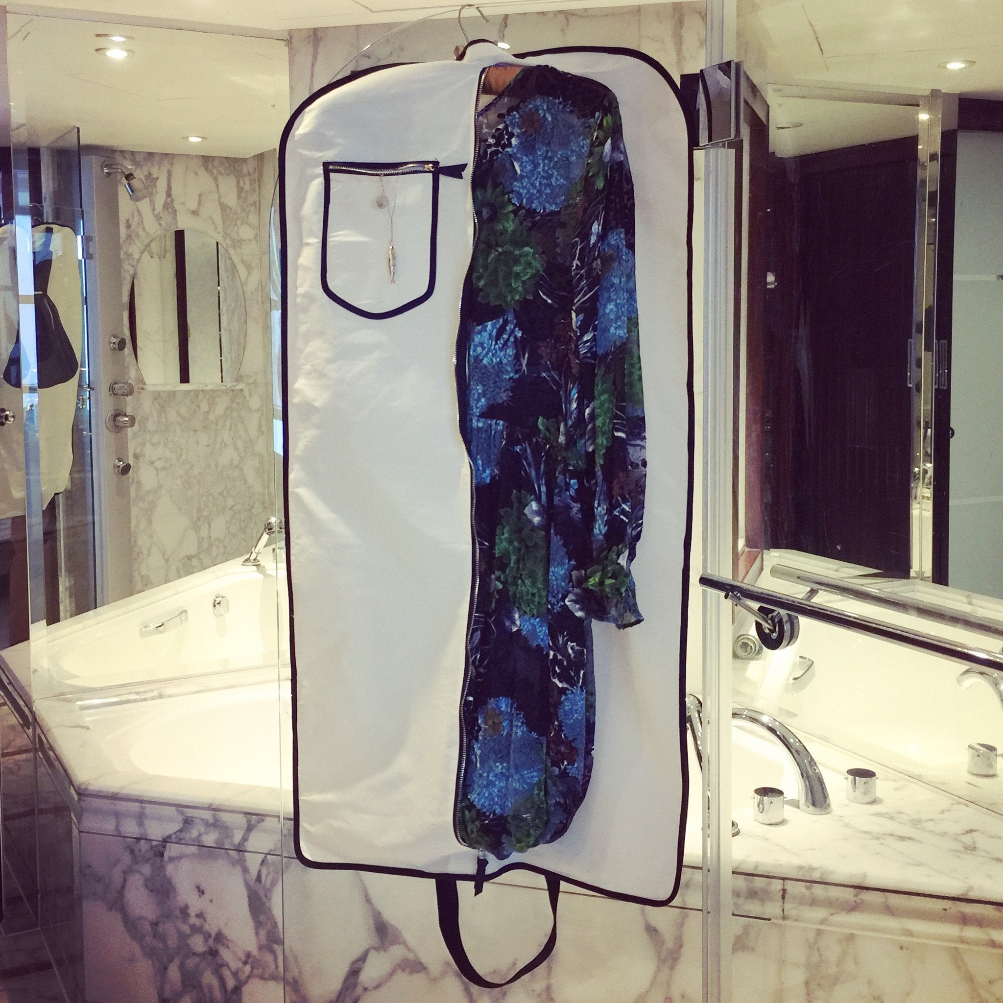 Une salle de bains en marbre avec une robe de sac à vêtements LBD accrochée à la douche.