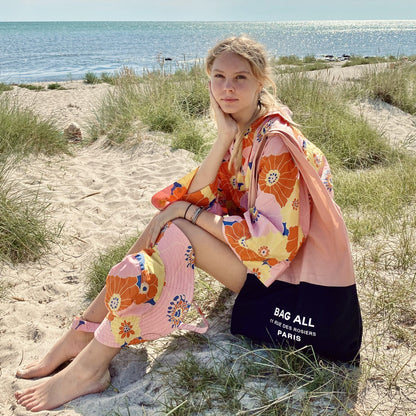 Une fille à la plage avec son tote bag rose et noir.