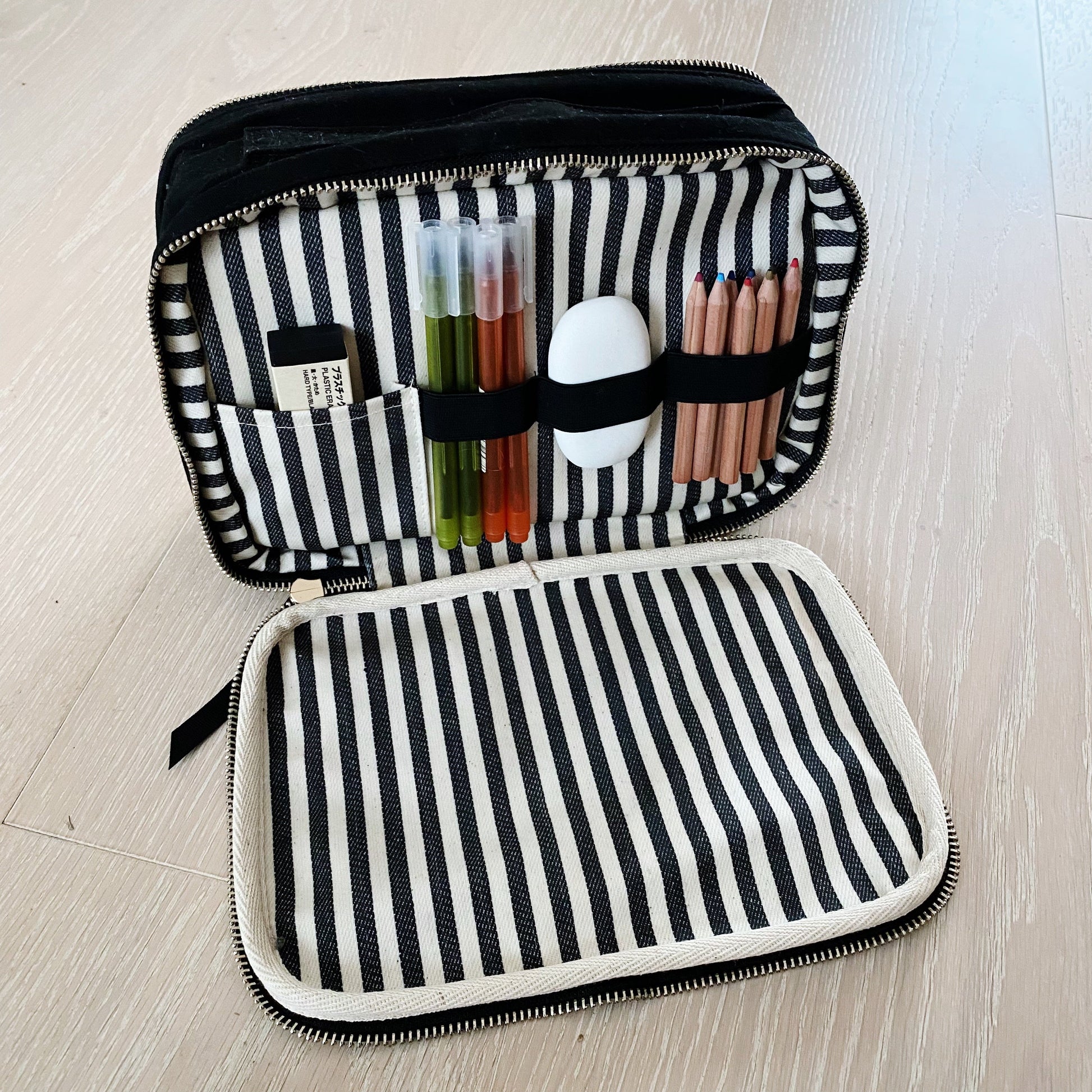 Bag-all Double Sided Multi Use Case in black with striped interior, featuring organized compartments holding makeup tools, pencils, and test tubes against a black and white striped cotton lining