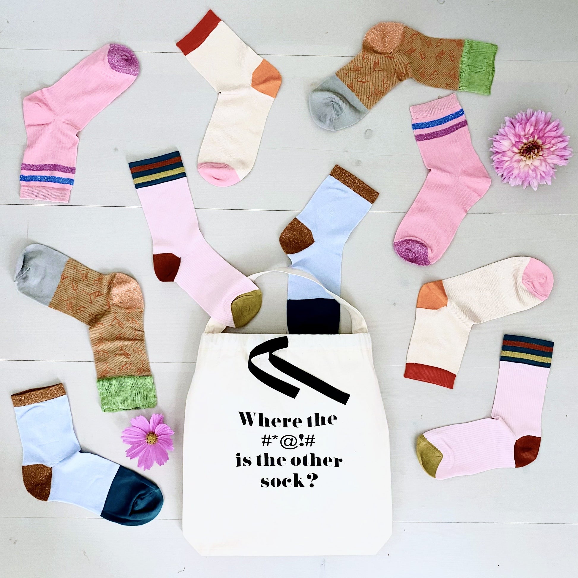 Bag-all Where Sock Bag in cream canvas with scattered colorful socks and pink flowers on white wooden surface, perfect for organizing mismatched socks and preventing lost pairs