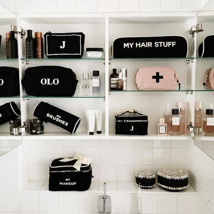 Bag-all Hair Stuff Travel Case in black displayed in organized bathroom shelving unit alongside matching beauty cases and toiletries, showcasing stylish storage solution for hair tools