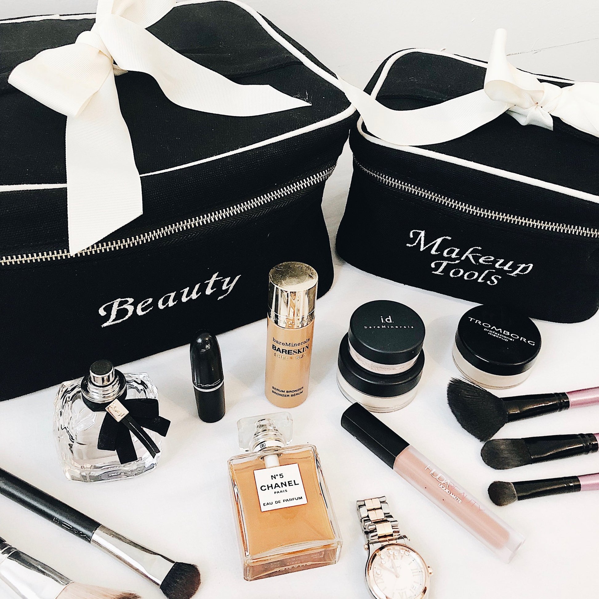 Bag-all beauty organizer cases in black with white bow, shown with makeup tools, perfume bottles and cosmetics. Monogram customization available for personalized storage solutions.