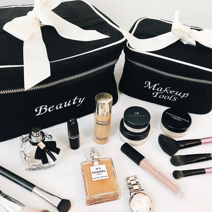 Bag-all beauty organizer cases in black with white bow, shown with makeup tools, perfume bottles and cosmetics. Monogram customization available for personalized storage solutions.