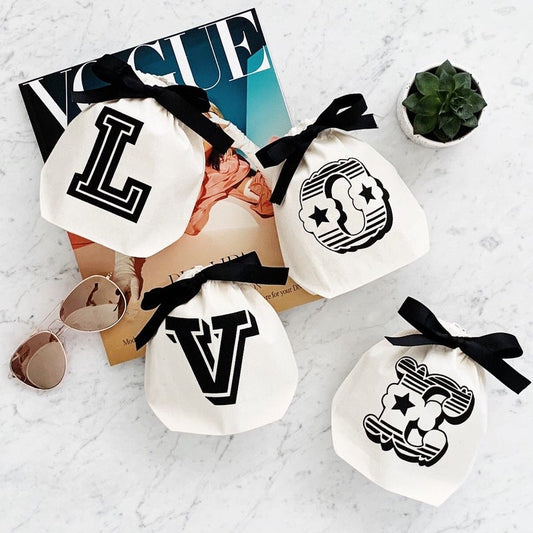 Bag-all Small Letter Bags Mix in cream cotton with black letter designs and ribbon ties, featuring stylish monogram prints and star patterns on marble surface with magazine and sunglasses