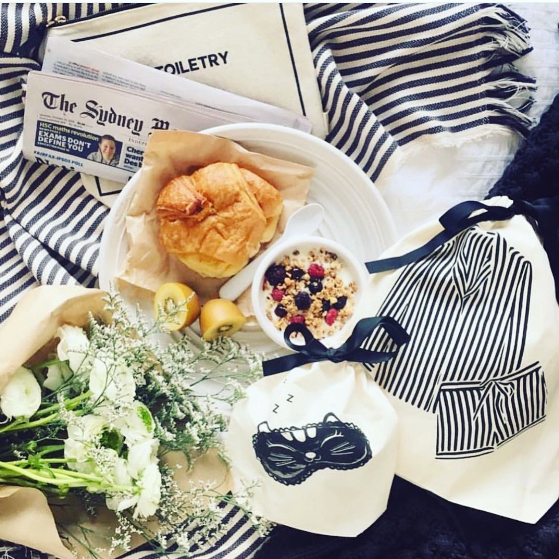 Bag-all Striped Pajamas Travel Bag in cream displayed with breakfast setting, fresh flowers, striped fabric, and travel essentials creating a cozy morning atmosphere