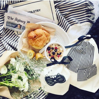 Bag-all Striped Pajamas Travel Bag in cream displayed with breakfast setting, fresh flowers, striped fabric, and travel essentials creating a cozy morning atmosphere