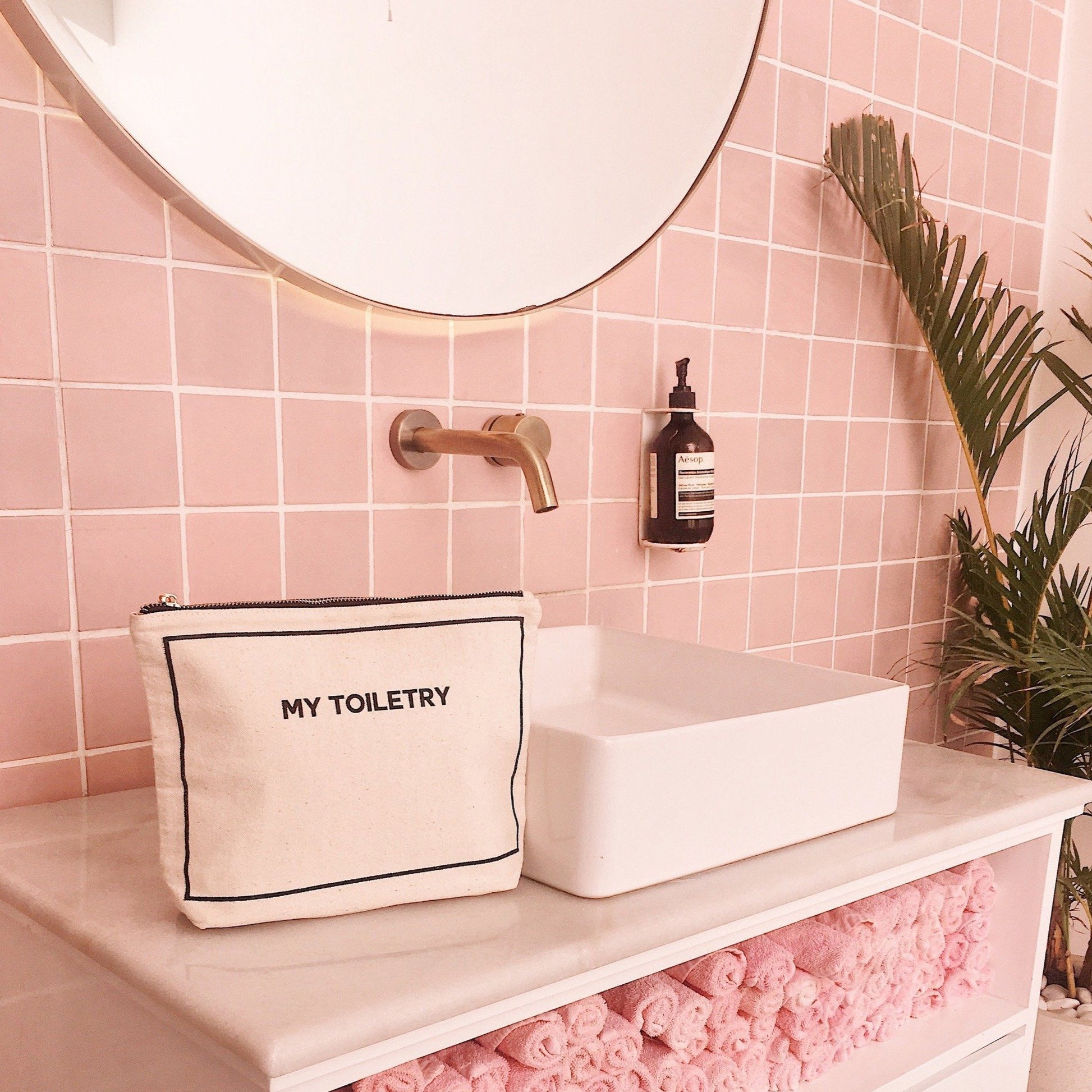 Bag-all Cream Toiletry Pouch with coated lining displayed in stylish bathroom setting with pink tiles, modern brass faucet and white vessel sink, showcasing waterproof design and organized storage